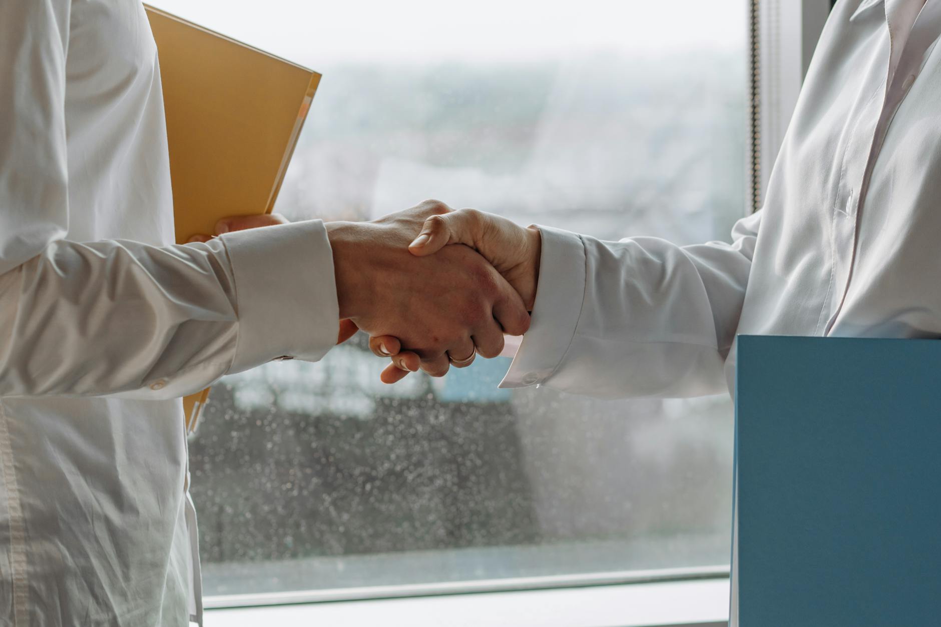 Two hands in business attire reaching across table in diplomatic gesture