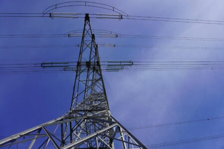 State Officials Challenge Utility Windfall From AI Power Demand High voltage transmission lines against blue sky